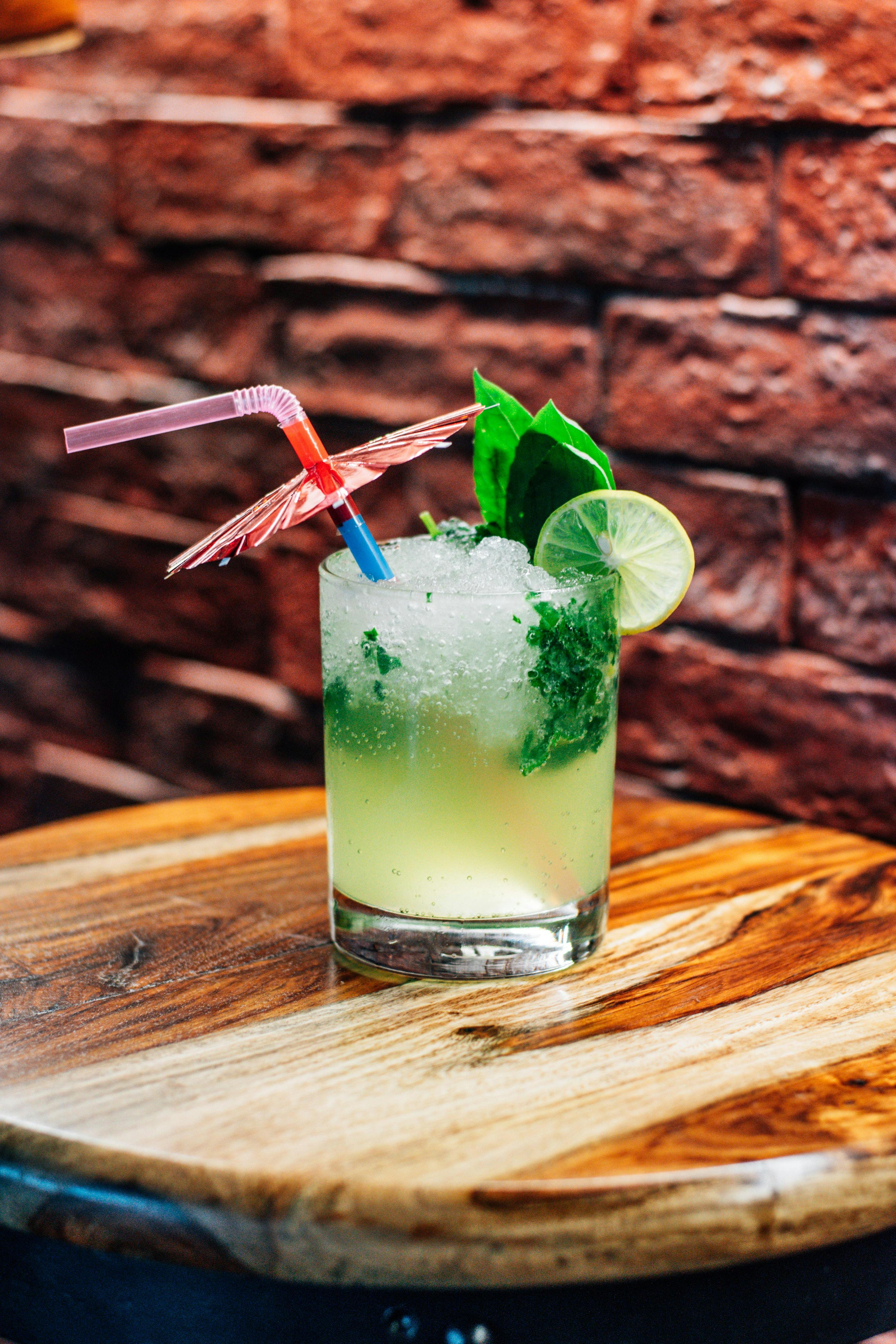 A mojito glass standing on a small round table in front of a brick wall. A straw and a small umbrella is sticking out of the drink.